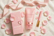 Mossicare Collagen Night Wrapping Mask – flat lay of pink product box, matching tube, and pink-handled applicator brush with gold ferrule on white textured fabric with scattered pink rose petals and a pink satin ribbon